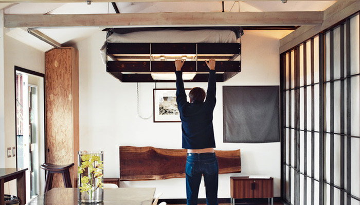 A man is pulling down a bed from the ceiling in a small apartment.