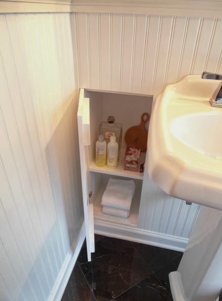 Built-in bathroom wall storage shelves are storing shampoo, conditioner, perfume, bar soap, a handheld mirror, and face towels.