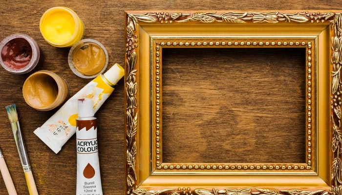 A freshly painted golden frame with paints and brushes on the side