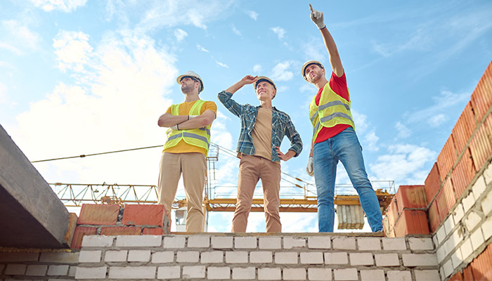 Men standing on a brick wall of a building under construction