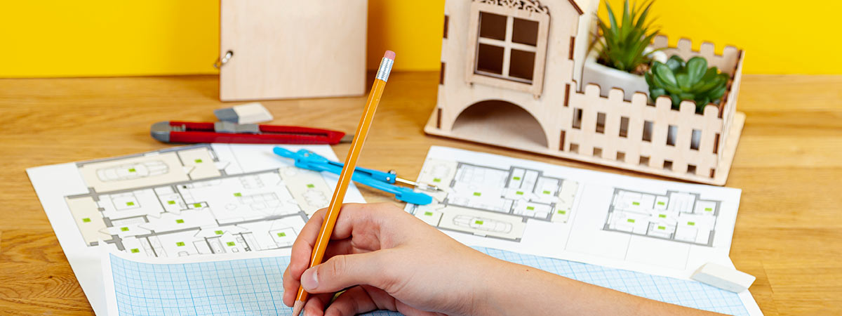 Working on the blueprints of a house on a table with a wooden model house