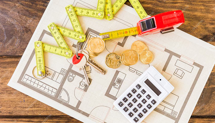 Flat lay shot of blueprint of a house on a table with measuring tape, calculator, coins, and house keys