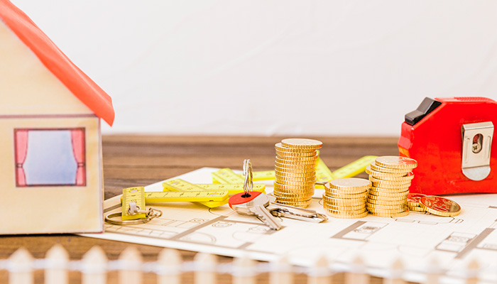 Blueprint of a house on a table with measuring tape, calculator, coins, house keys and a model house